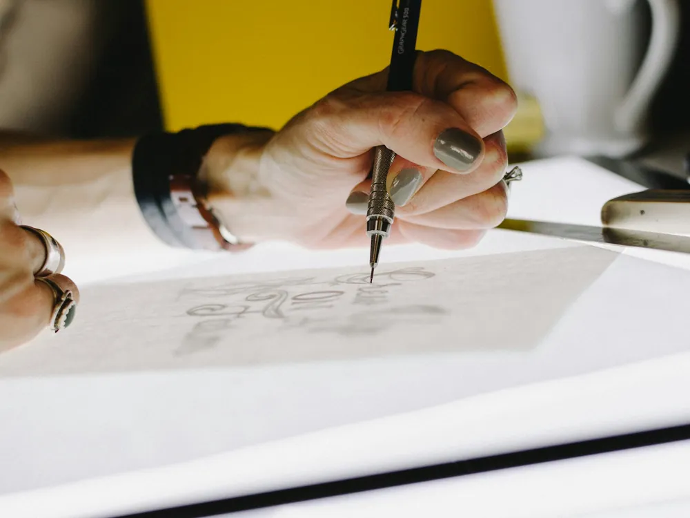 A hand drawing a design on tracing paper