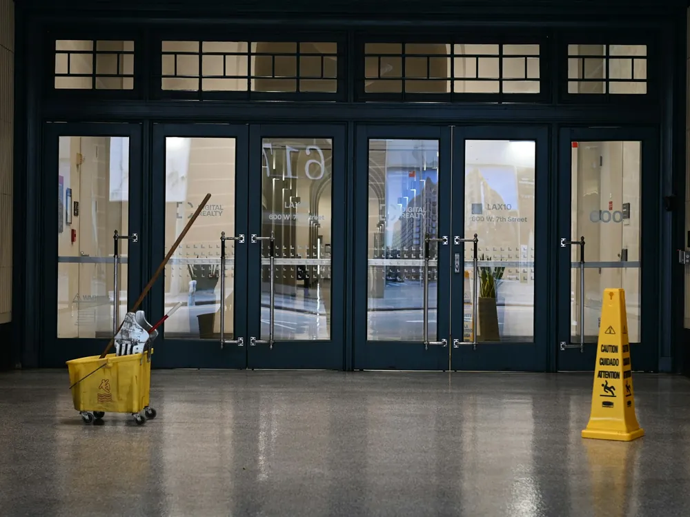 A mop bucket and a wet floor sign by glass doors