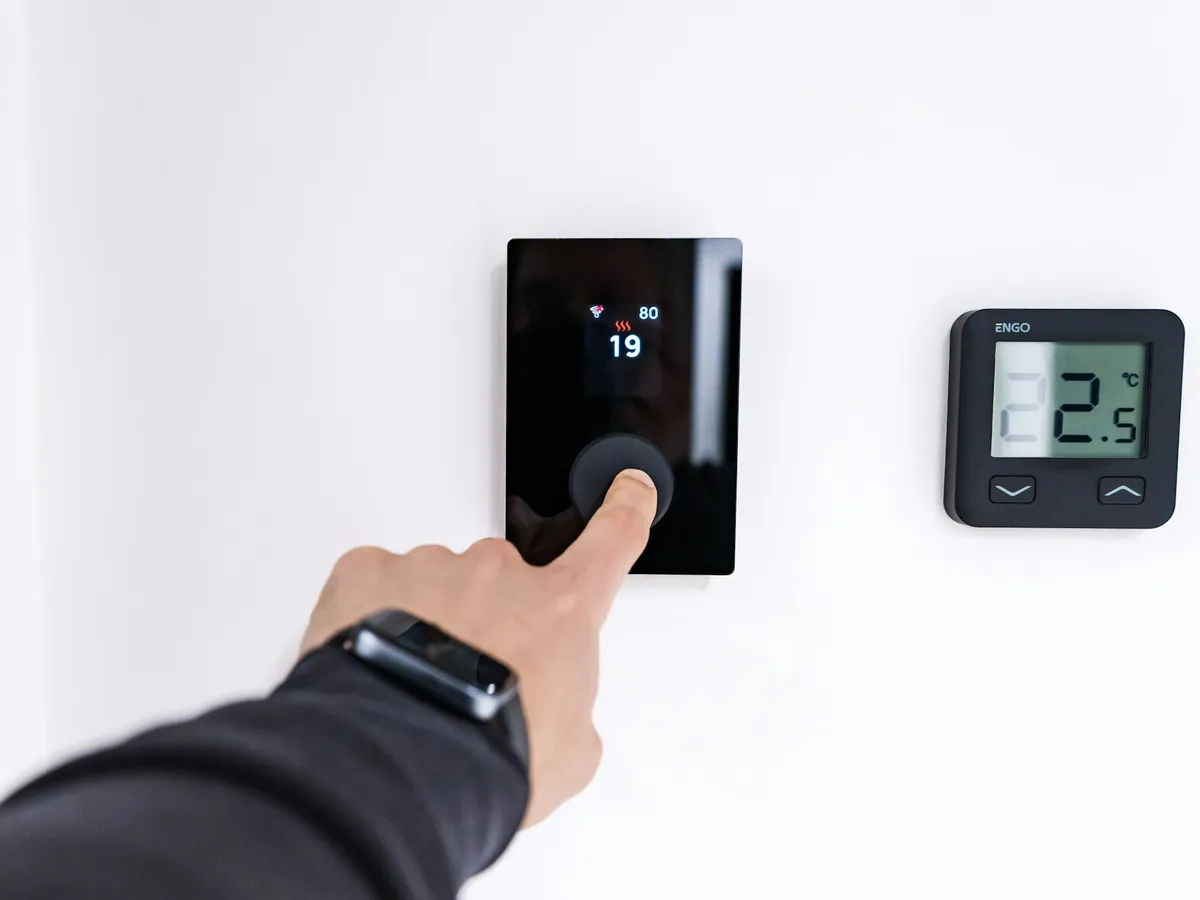 A finger setting a wall thermostat