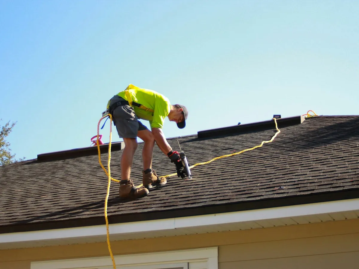 A roofer fastening shingles with a drill
