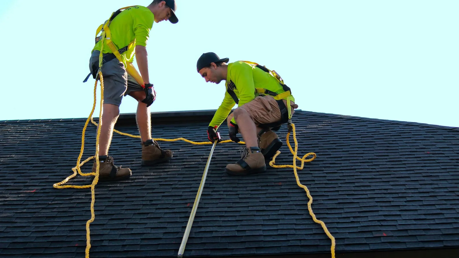 Two roofers working on a dark shingle roof